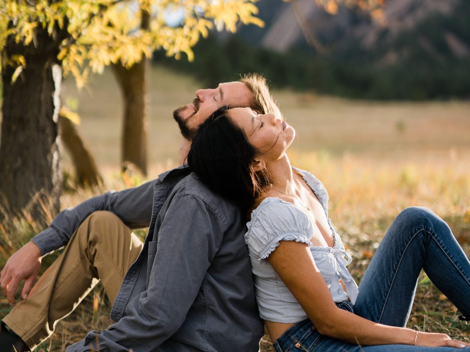 cute aesthetic couple sitting in a field leaning against each other during their Chautauqua engagement photos