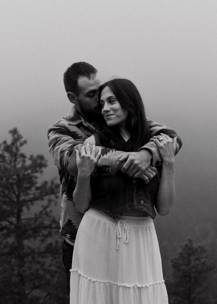engaged couple standing on a rock kissing in the middle of field during a storm in colorado