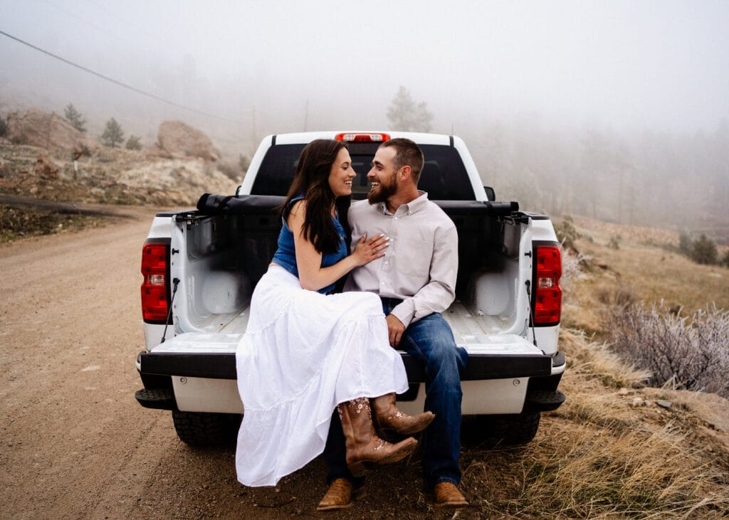 cute country couple sitting in the back of the pickup truck during their proposal in colorado