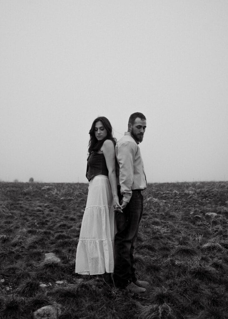 engaged couple standing back to back holding hands in a field during their colorado engagement session