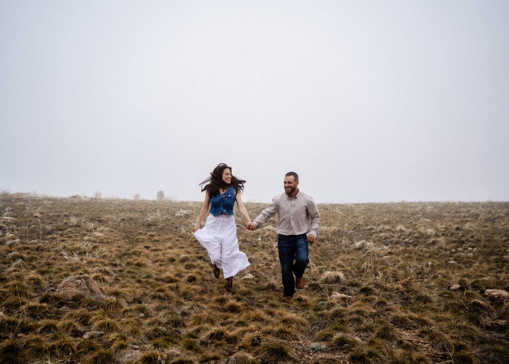 cute newly engaged couple sitting in a field together kissing during their colorado engagement session