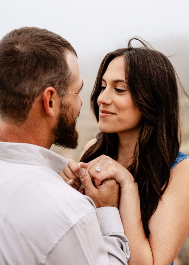 cute engaged couple looking at each other as he brings her hands up to his face during their proposal in colorado