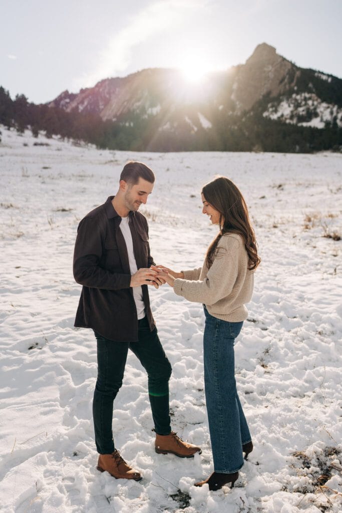 Boyfriend putting engagement ring on girlfriends finger after he proposed at Chautauqua Park in Boulder, Colorado during their winter engagement session