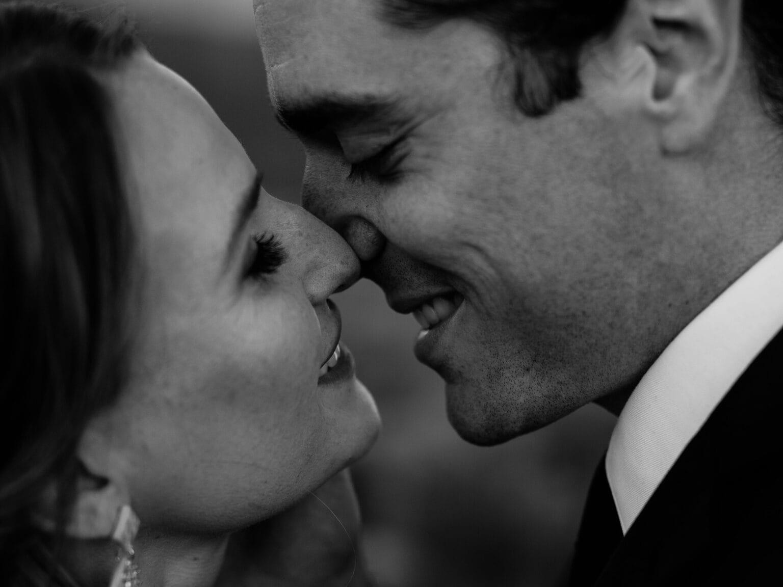 A close-up, black and white photo of a couple smiling lovingly, touching their noses together with their eyes closed, expressing affection and intimacy.