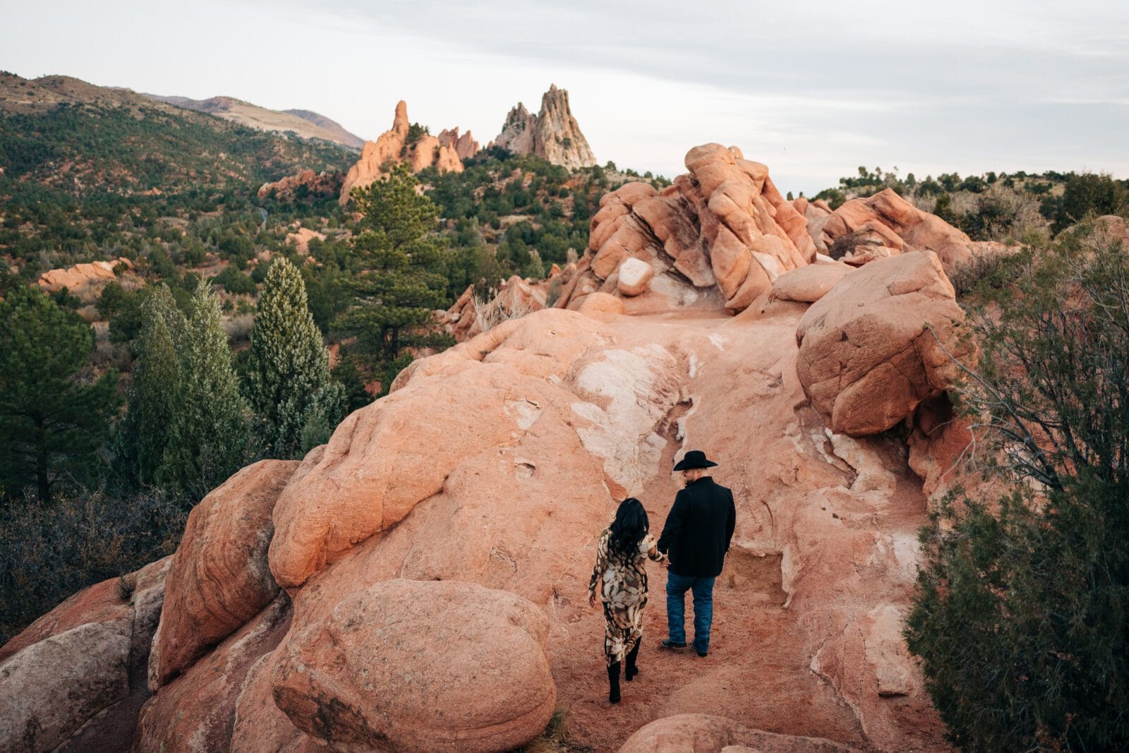 Couple walking together during a Garden of the Gods photoshoot at sunrise with red rock formations in the background.