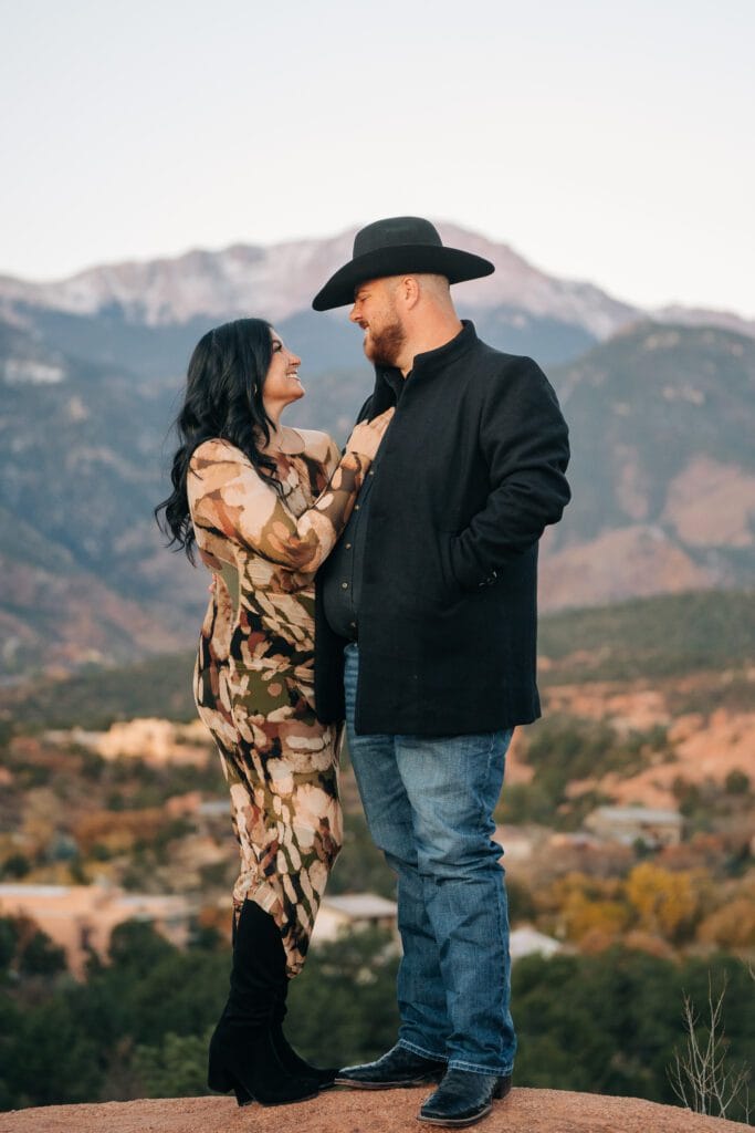 girlfriend putting her hand up on her boyfriends chest while they smile at each other with pikes peak in the background during  their garden of the gods photoshoot