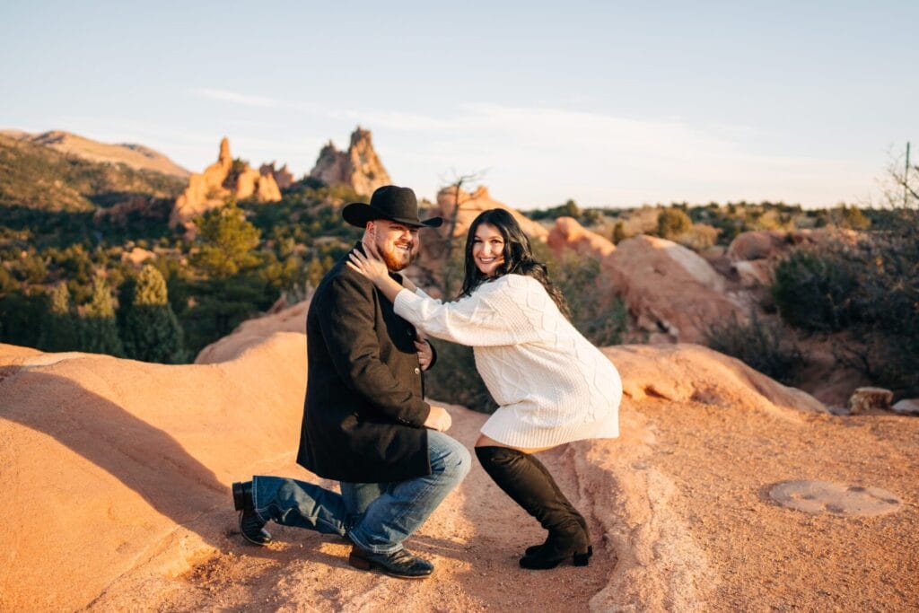 girlfriend crouching down to her boyfriend as he proposes to her during their garden of the gods photoshoot