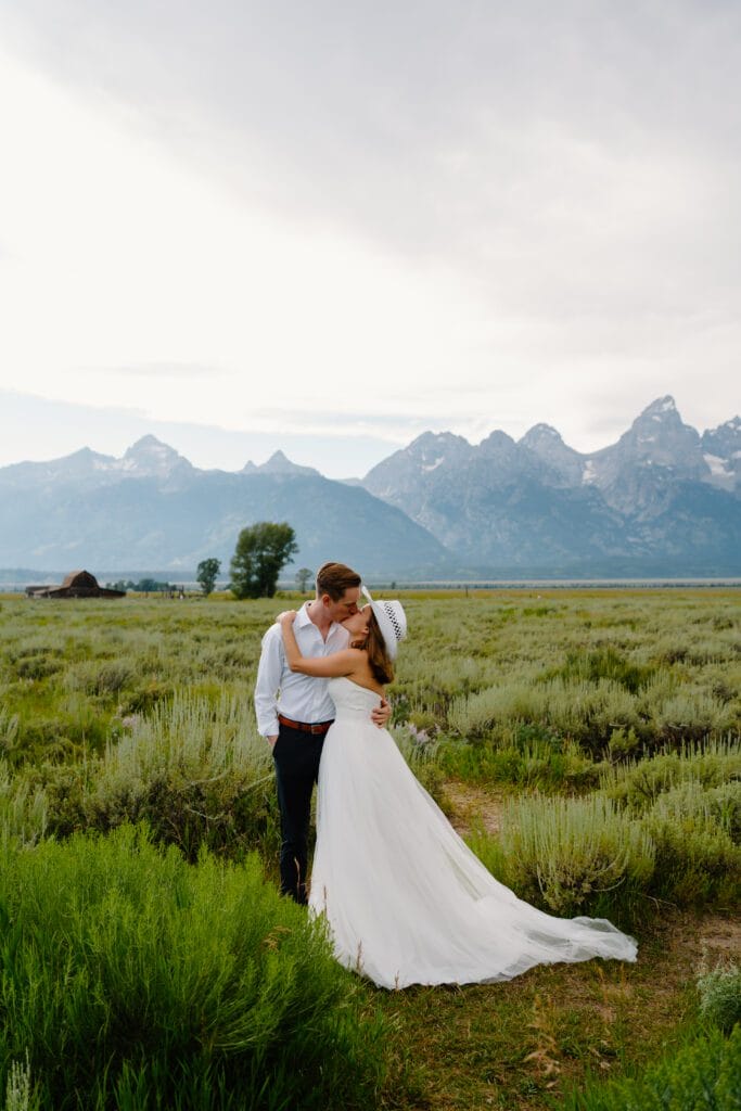 married couple kissing in a field in front of the grand tetons in their wedding attire during their wyoming elopement