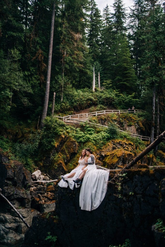 brides sitting on a cliff together after their wedding ceremony in mt rainier national park during their washington elopement
