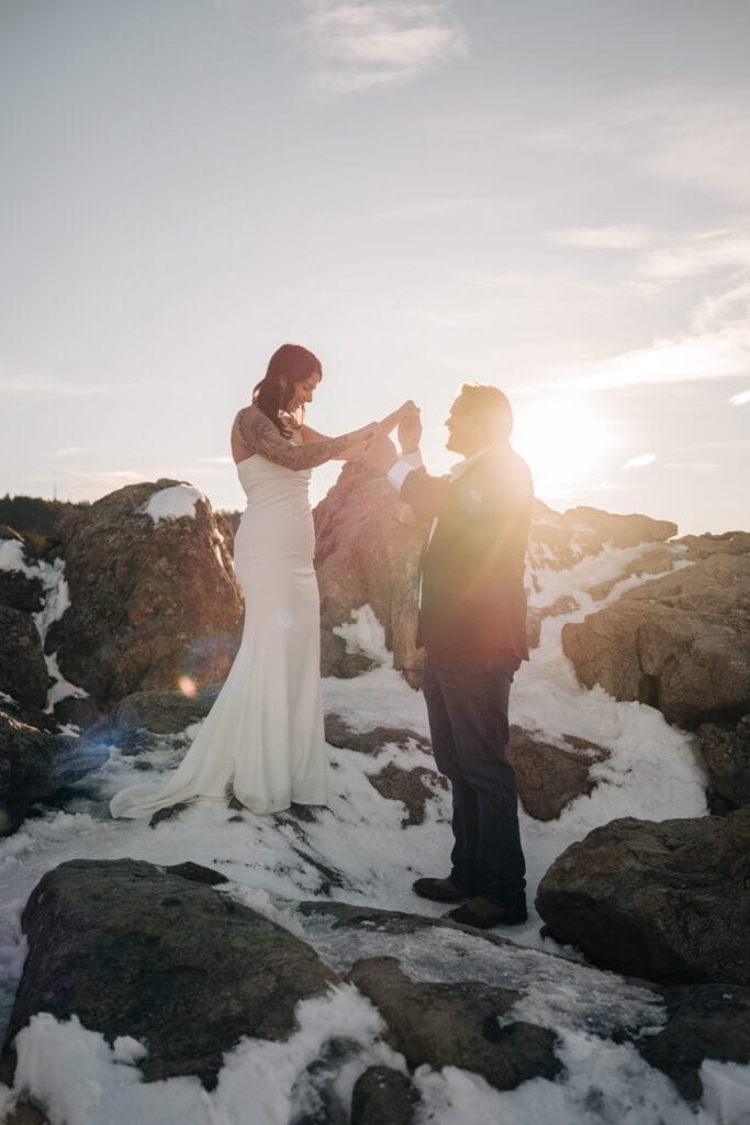 groom holding brides hands up as the camera catches a sun flare during their sunset boulder elopement