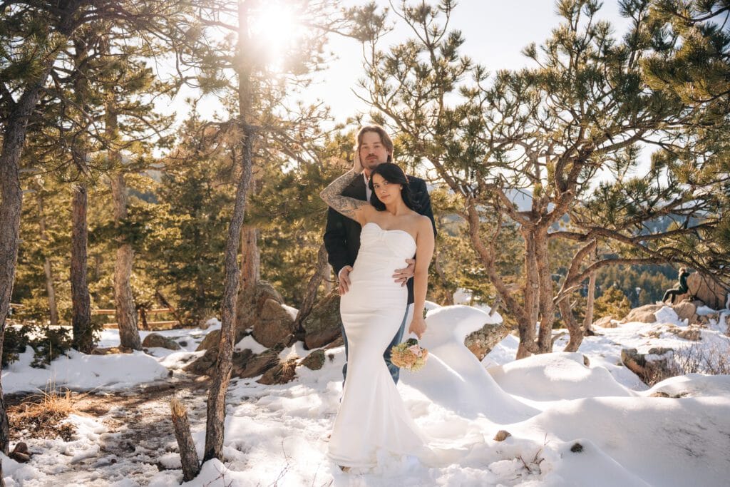 groom holdig bride from behind as they look at the camera in the forest a Lost Gulch Overlook during their Boulder elopement in Colorado
