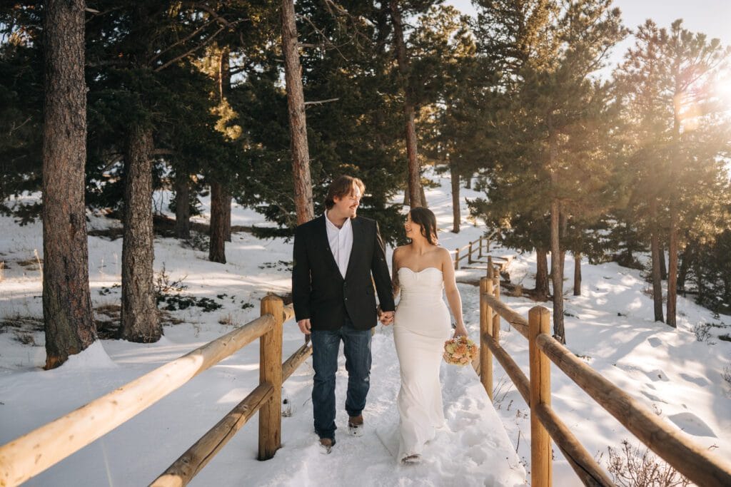bride and groom holding hands walking down a path in the snow covered forest at Lost Gulch Overlook during their boulder elopement in colorado