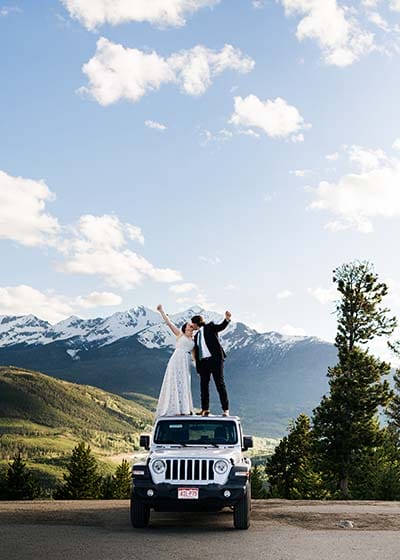 Couple celebrating on SUV with mountain backdrop