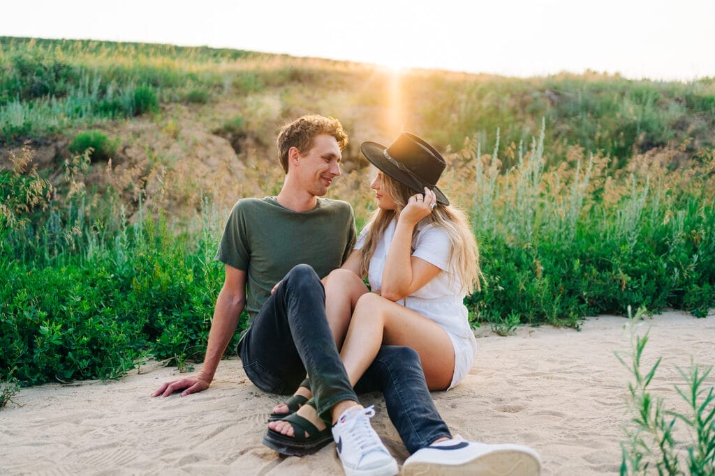 Couple sitting on sand at sunset smiling