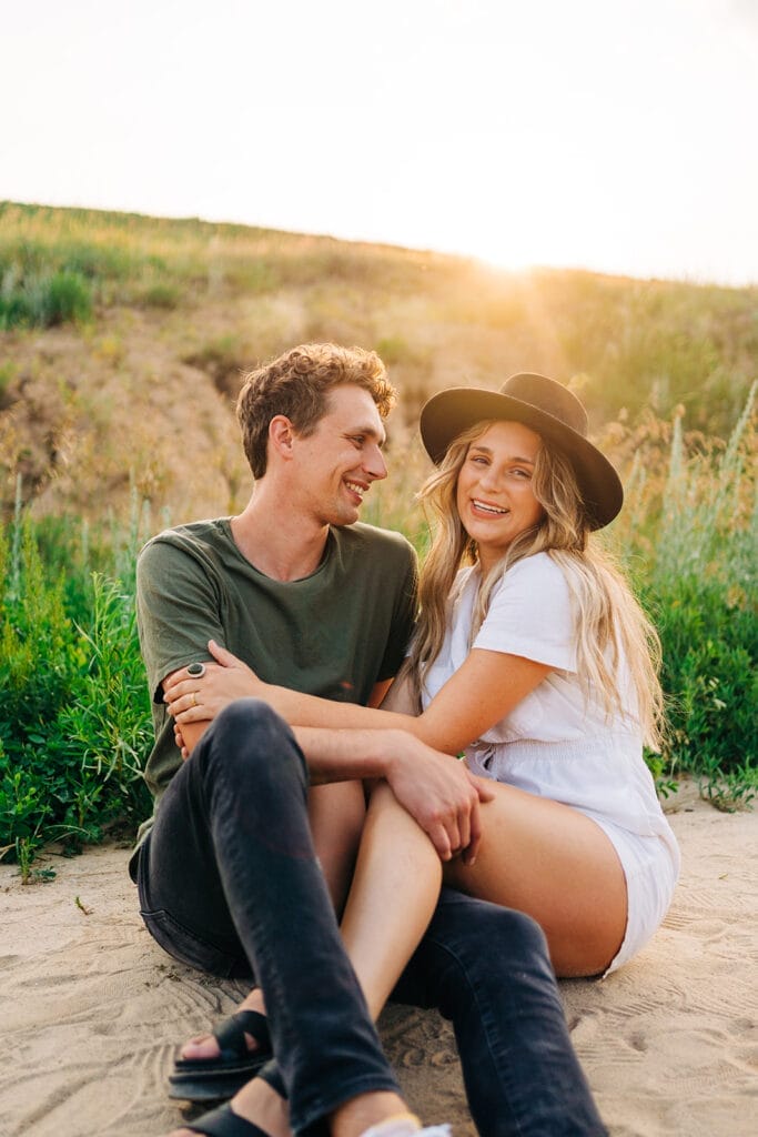 Couple sitting in a grassy field smiling at each other during their couples photoshoot at the Colorado Paint Mines