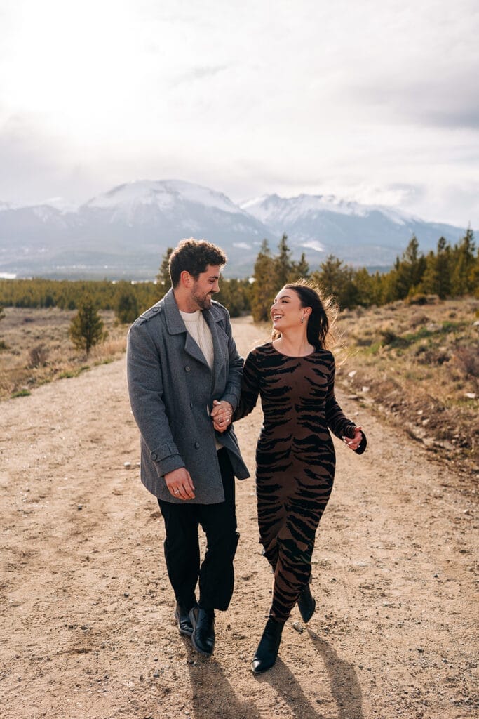 Couple walking on mountain path, smiling at each other during Sapphire Point engagement