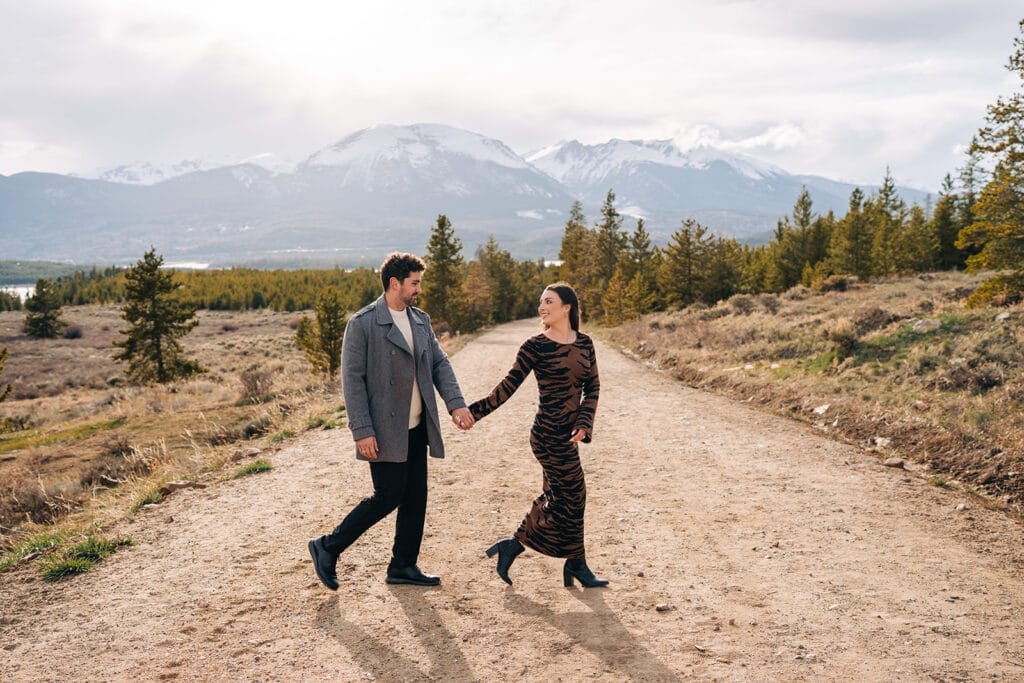 Chelsea and Eric holding hands and walking down a path together at Sapphire Point Overlook in Breckenridge, CO