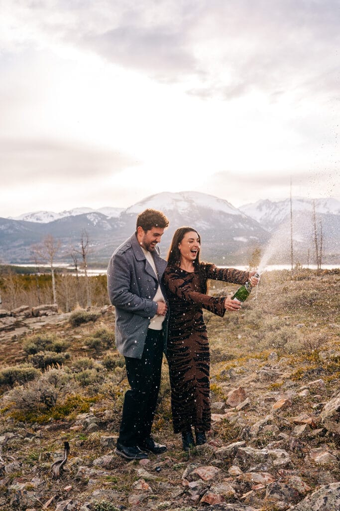 Chelsea spraying champagne as her fiance smiles at her during sunset at Sapphire Point Overlook