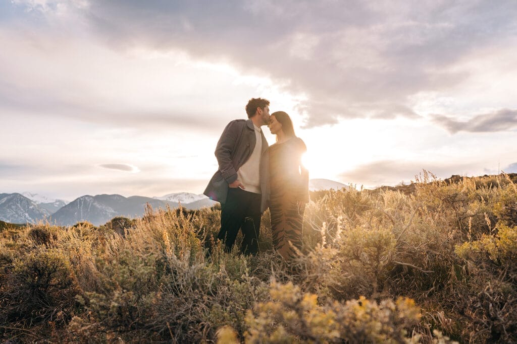Eric kissing Chelsea's forehead in a meadow at Sapphire Point Overlook during sunset