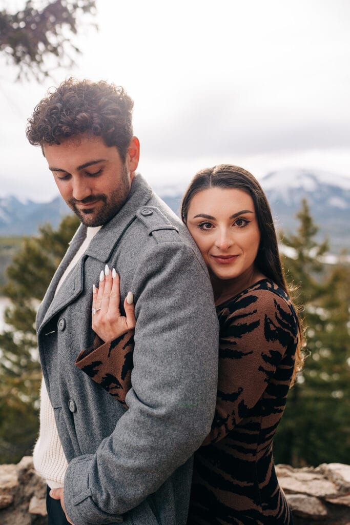 Chelsea smiling at the camera as she hugs Eric from behind as he looks down at her, showing off her new engagement ring after their proposal at Sapphire Point Overlook in Breckenridge, CO